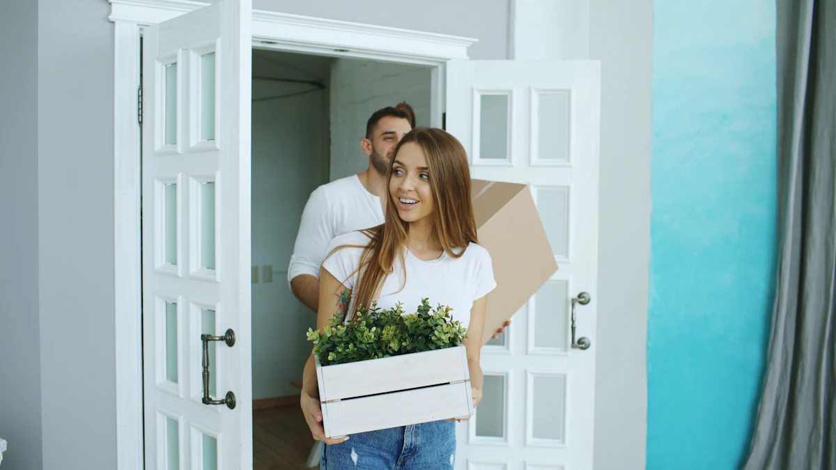 Couple carrying moving boxes and a plant into a new home